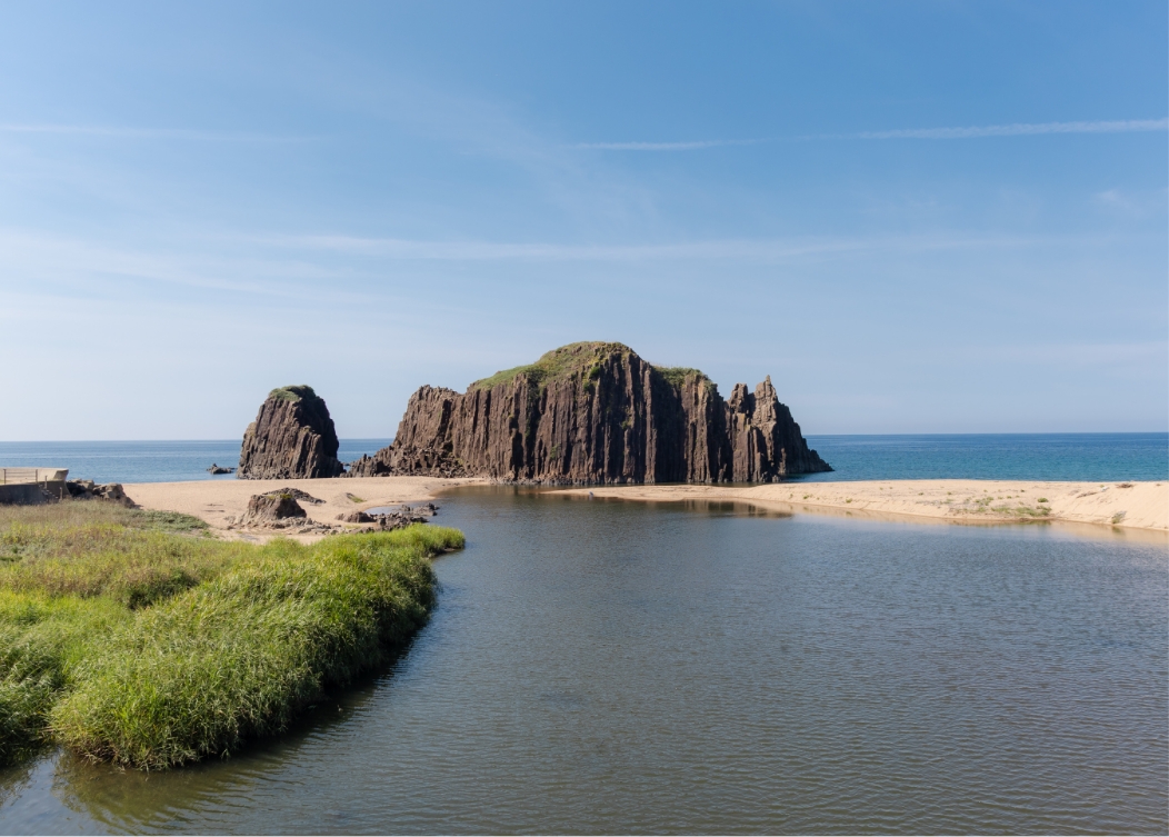 京都府丹後地方の、砂浜と川、そして海にそびえ立つ岩